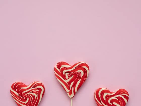 sweet lollipops in form of hearts against pink background